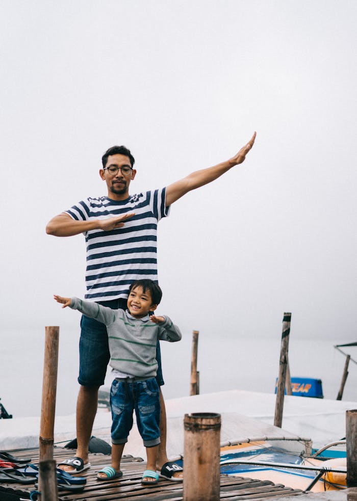 services-01 Father and son posing playfully on a wooden dock by the water, enjoying a day outdoors.