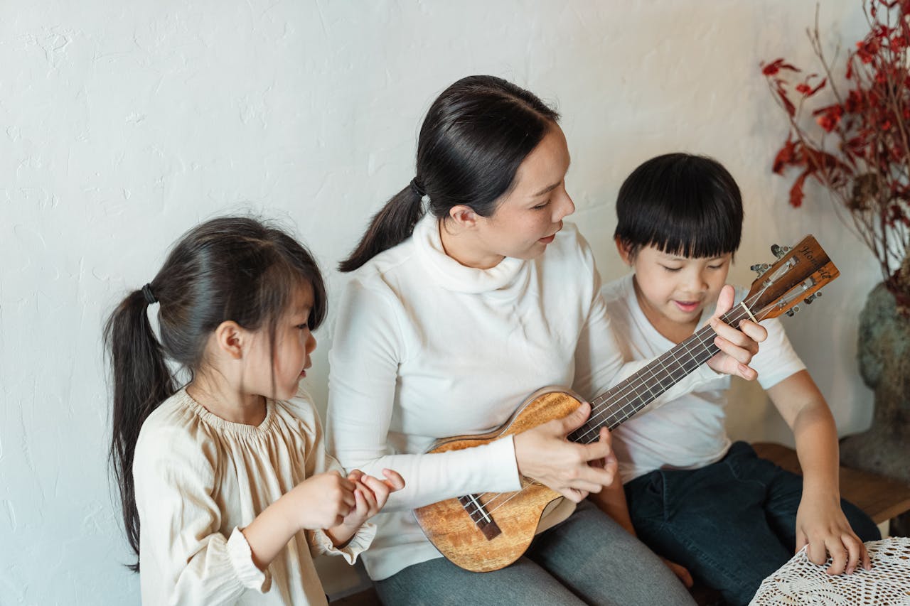 Mastering the First Impression: Your intriguing post title goes here A mother teaches her children to play the ukulele indoors, creating a warm and joyful family moment.