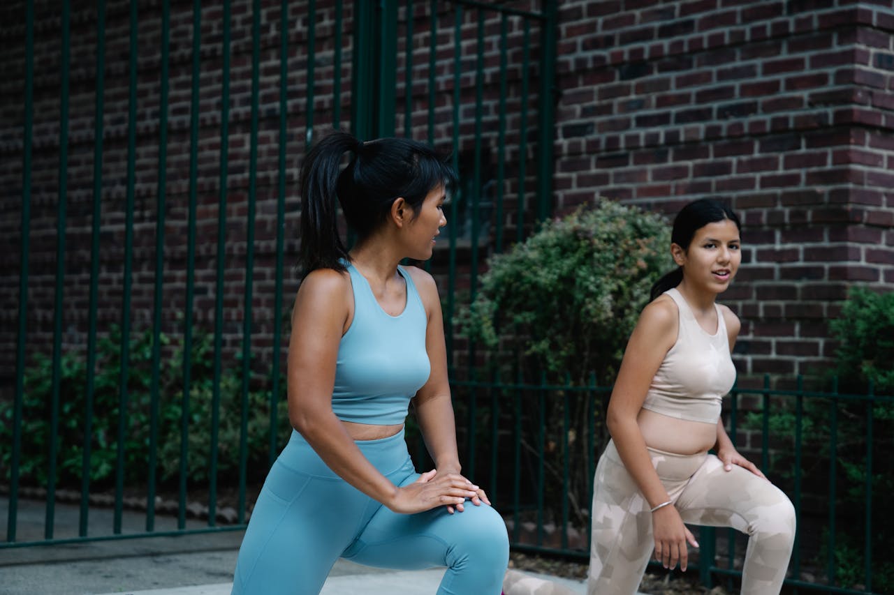 about-us Mother and daughter stretching on the sidewalk in sports clothing, focused on fitness.